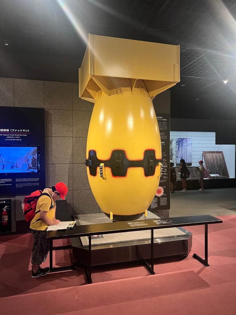 Een hangend, dik geel/rood model van een bom, tegen een zwarte achtergrond.