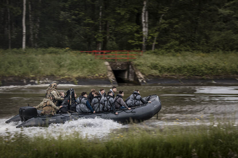 2 Belgische militairen besturen een rubber motorbootje met daarin een groepje jongeren.