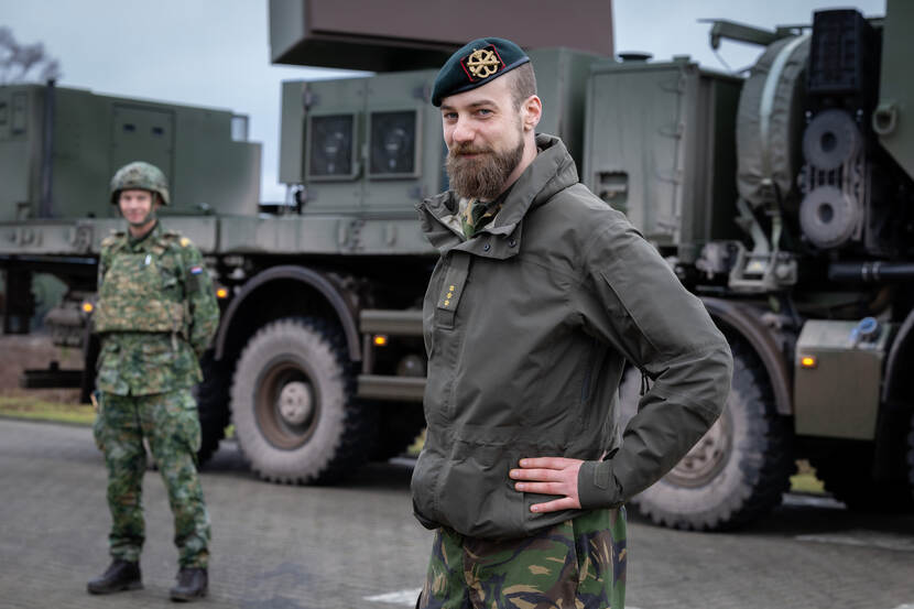Twee militairen poseren voor de Ground Master, met het artillerieschietkamp op de achtergrond.