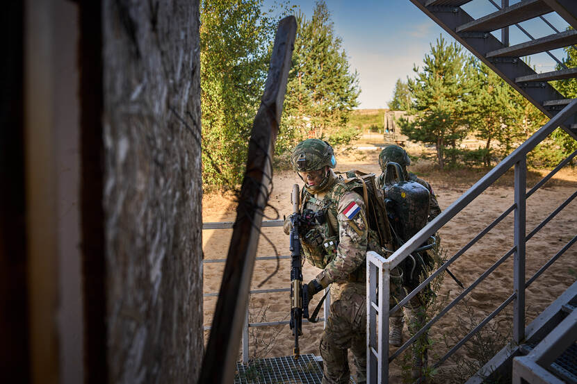 Twee militairen staan klaar voor een trappenhuis in Litouwse namiddagzon, gereed om het gebouw binnen te gaan.
