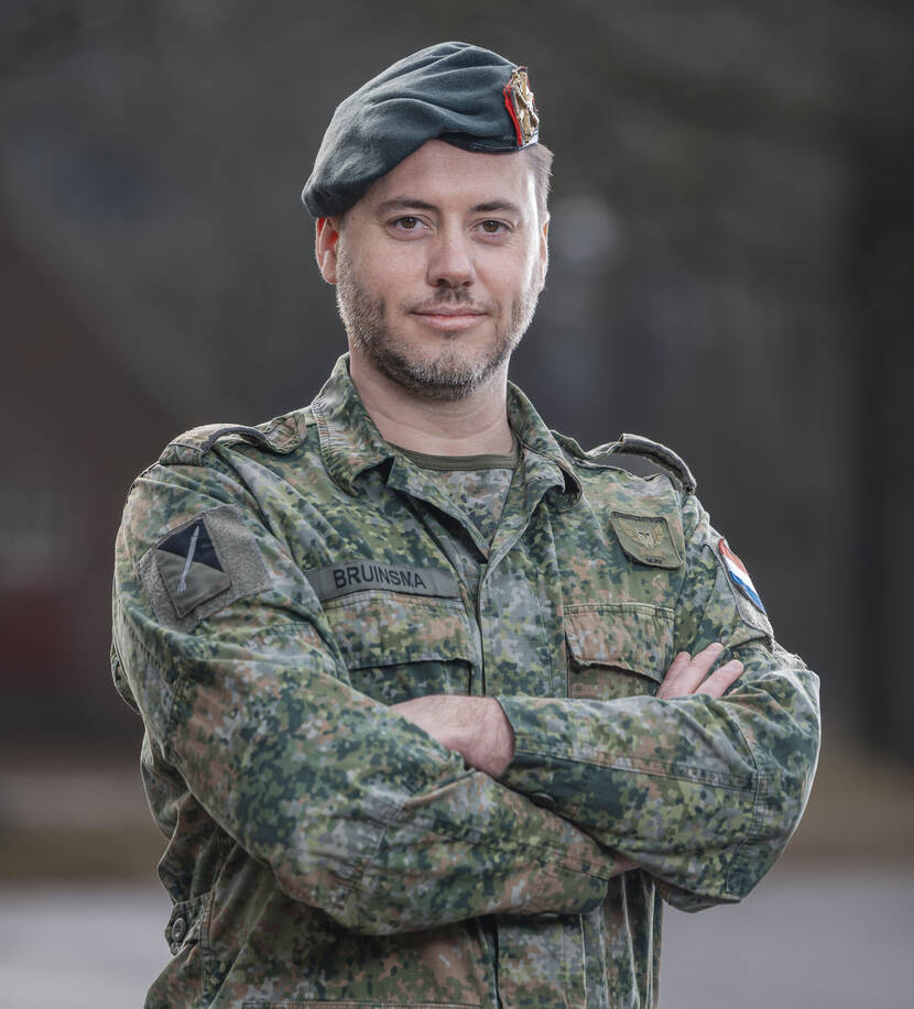 Een majoor in militaire outfit poseert lachend en met armen ober elkaar
