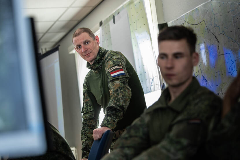 2 militairen – 1 staand en 1 zittend – bevinden zich achter een scherm.