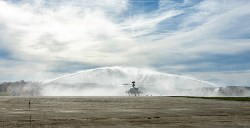 Twee brandweerwagens spuiten een waterboog waaronder de Apache door taxiet.