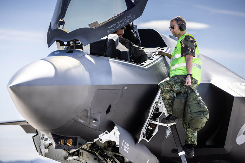 een militair reikt de helm aan van een vlieger die in de cockpit van een F35 zit.