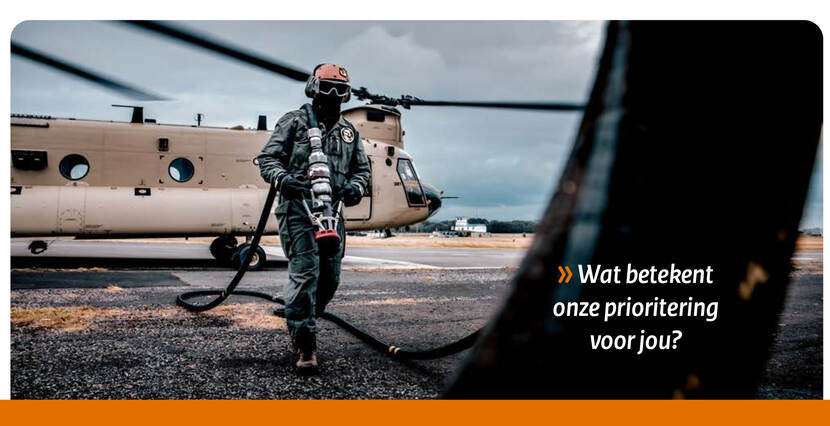 Een militair met helm en masker op sjouwt een tankslang terug naar de tankwagen. Op de achtergrond een Chinook. In de foto staat de tekst: Wat betekent onze prioritering voor jou?