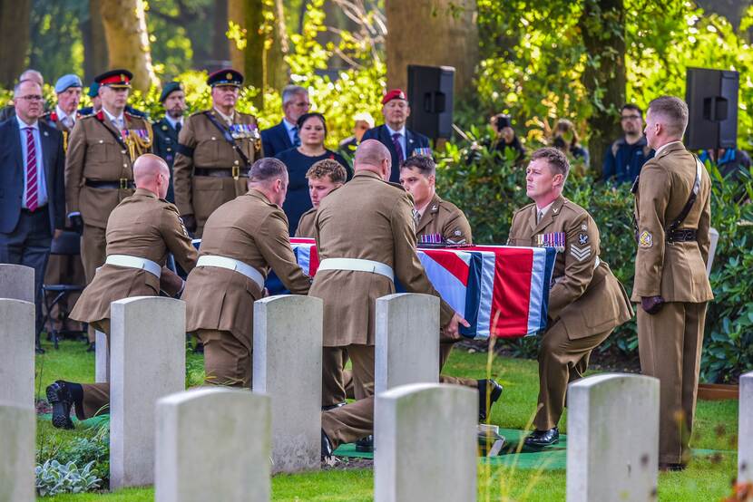 Militairen laten een kist met daarop een Britse vlag zakken in een graf.