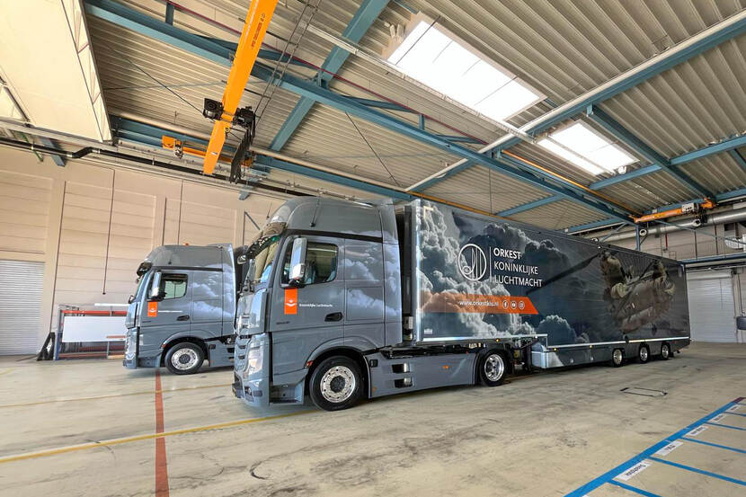 Twee nieuwe vrachtwagens van het KLu-orkest staan naast elkaar in een hangar.