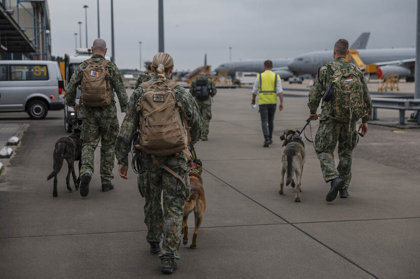 Militaire bewakers met honden lopen richting het vliegtuig.