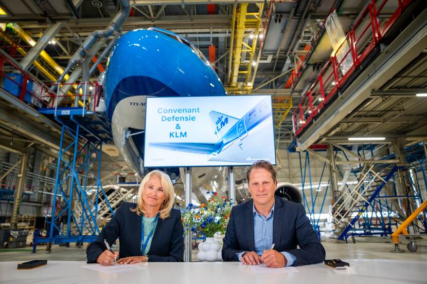 President-directeur Marjan Rintel en staatssecretaris Gijs Tuinman aan een tafel. Achter hen een KLM-Boeing 777.