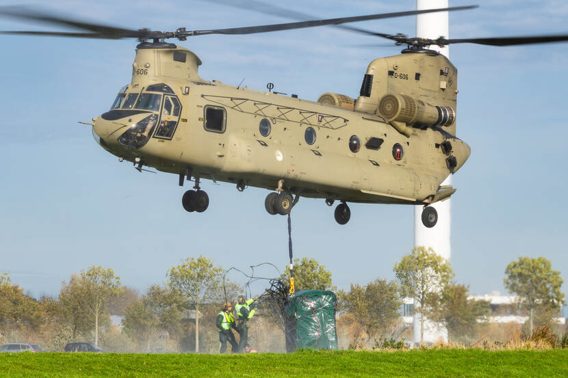 Militairen hangen een groot groen pakket onder een vliegende Chinook.