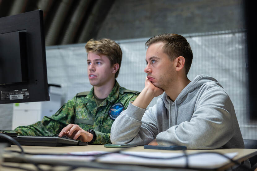 Een jonge mannelijke militair en een leeftijdsgenoot in burgerkleding kijken naar een computerscherm.