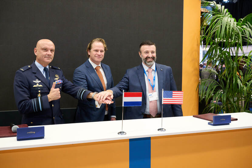 Commandant Lucht- en Ruimtestrijdkrachten legt vanachter een hoog bureau de handen op elkaar met de staatssecretaris van Defensie en een civiele samenwerkingspartner.