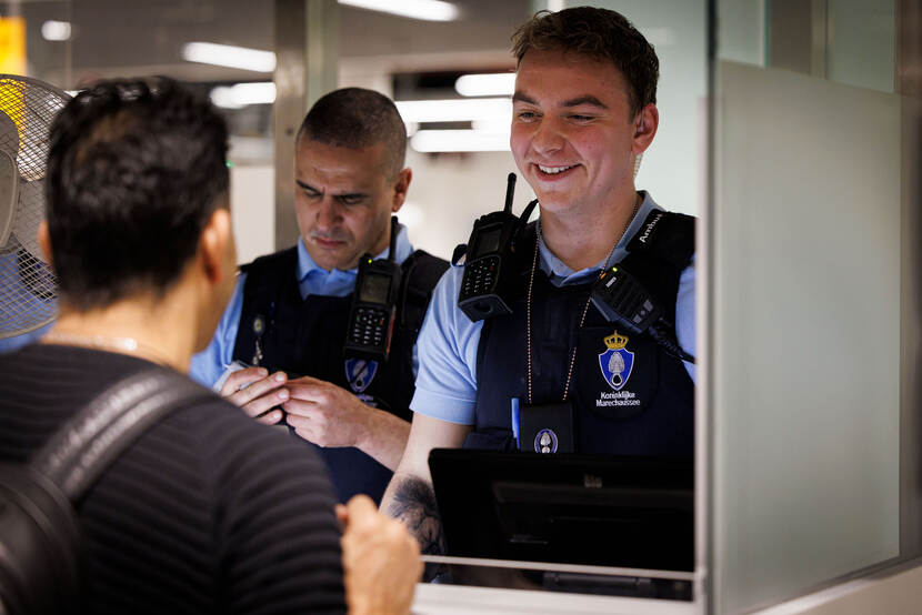 Een collega controleert een document van een reiziger.