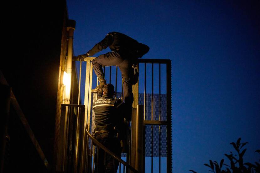 De Marechaussee doet een instap in een woning door over een hek te klimmen.