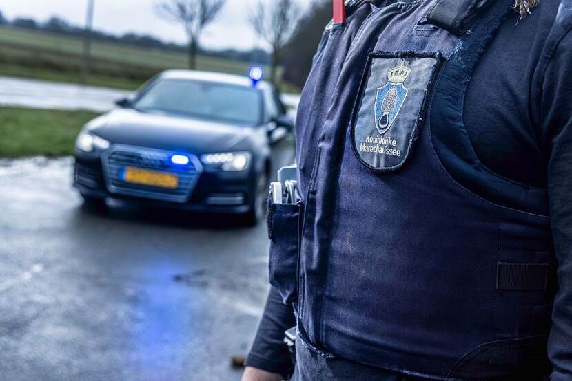 Marechaussee staat voor zijn wagen waarmee hij controles uitvoert.
