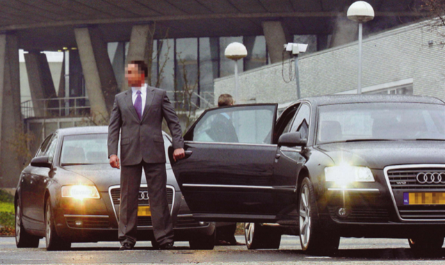 Persoonsbeveiliger in net pak houdt autodeur open en houdt de omgeving in de gaten.