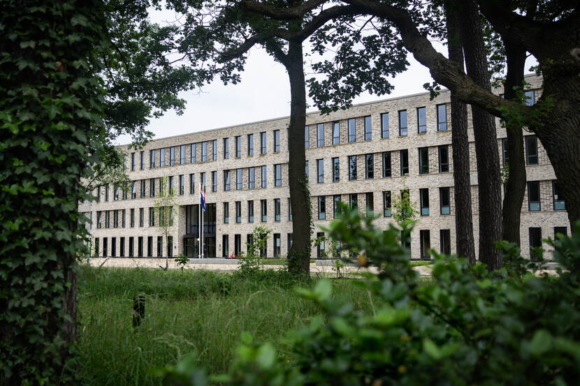 Een doorkijkje via de bomen naar het nieuwe, zandkleurige kantoorcomplex van het LTC.
