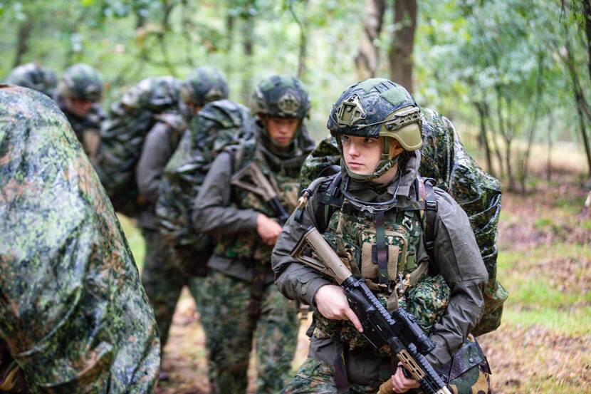 Een peloton dienjaarmilitairen loopt met volle bepakking en geweer een patrouille.