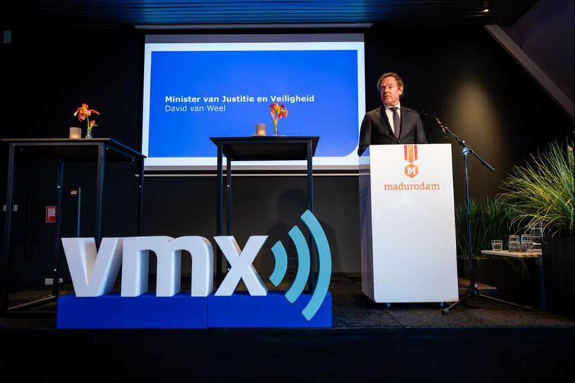 Minister van Weel staat op een podium voor het VMX-logo