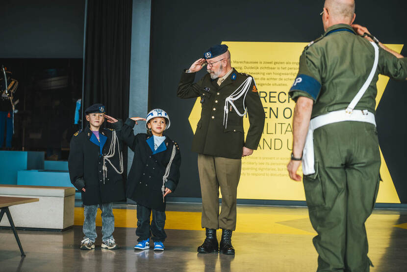 Marechaussee-veteraan salueert met twee kindjes naast zich die mee-salueren.