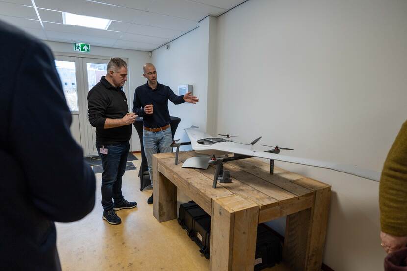 Twee mannen staan in een ruimte en kijken naar een witte drone met propellers.