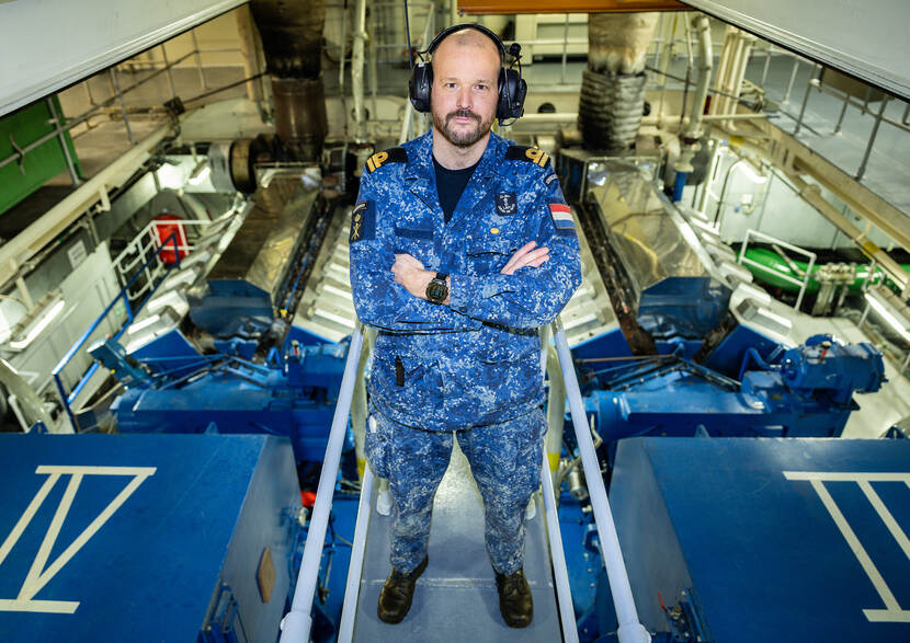 Militair van de marine staat in uniform met de handen over elkaar in machinekamer marineschip.