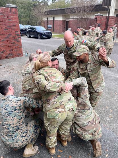 Zes militairen staan door elkaar heen met hun handen vast en moeten proberen om zichzelf los te krijgen.