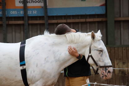 Een man met z’n hoofd tegen het hoofd van het paard en met zijn armen om de hals van het dier.
