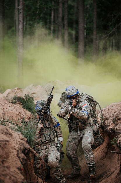 Twee militairen lopen met hun wapen in de aanslag door een loopgraaf.