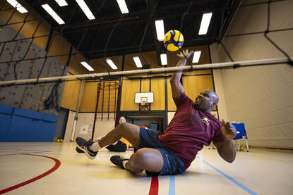 Sporter slaat een bal over het net tijdens zitvolleybal.