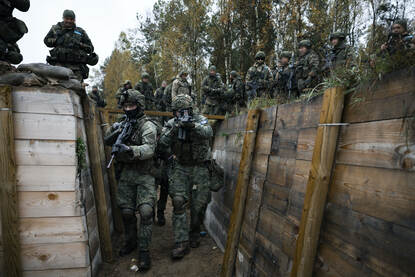 Twee militairen met wapens in de aanslag zuiveren een loopgraaf. Boven kijken andere militairen toe.