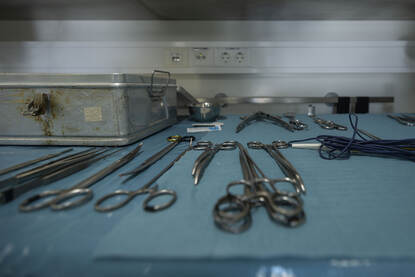 Een tafel met daarop verschillende scharen, pincetten en scalpels die gebruikt worden in het ziekenhuis. Deze liggen op blauw papier.