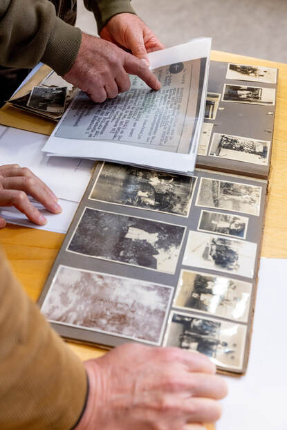 Een hand wijst op een document, met daarnaast een fotoalbum.