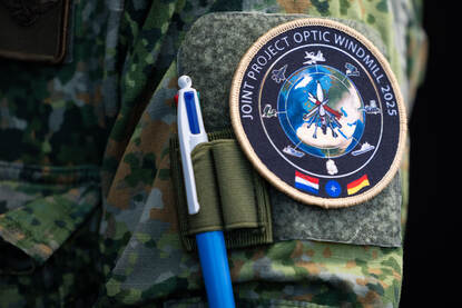 Het embleem van JPOW op de mouw van een militair. Daarop is een wereldbol te zien met in het midden verschillende typen raketten. Onderaan staan de vlaggen van de organiserende landen Duitsland en Nederland.