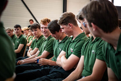 Links: Studenten zitten op een rij naast elkaar. Een van hen leest een vraag op van een briefje. Rechts: Twee militairen zitten met presentator op podium in zaal vol studenten.