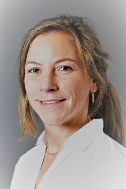 Pasfoto van vrouw met blond haar en witte blouse die lachend in de camera kijkt.