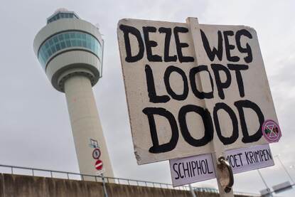 Links een protestbord met de tekst ‘Deze weg loopt dood’, rechts silhouetten van twee Marechaussees met op de achtergrond een matrixbord met de tekst ‘Demonstreren op Schiphol Plaza is verboden’.