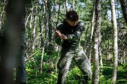 Een militair hakt een boom om terwijl een ander dennentakken verzamelt.