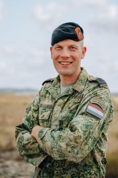 Militair met baret op kijkt lachend in de camera met de armen over elkaar.