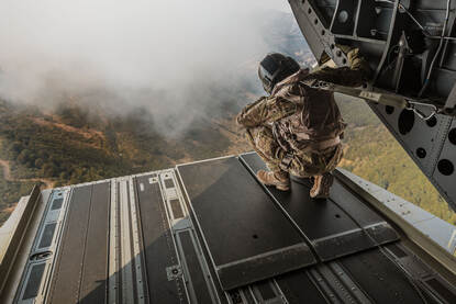 Een loadmaster kijkt vanuit de laadklep van een Chinook naar de bosbranden beneden.