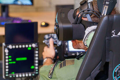 Militairen zitten met een VR-bril op achter een nagemaakte stuurknuppel van een Apache.