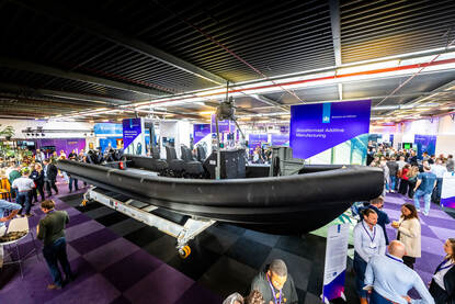 Links: Mannen in pakken staan rond een zwart bootje en een groot bord. Rechts: van bovenaf een inkijk in een grote zwarte boot.