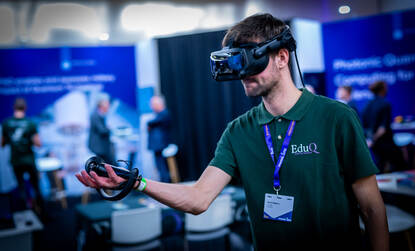 Links een man met een vr-bril op en een groen shirt aan. Rechts drie jongemannen zitten rond een schaakspel in een grote zaal.