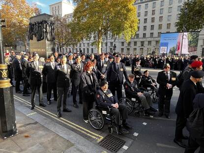 Links: Een groep veteranen in uniform, sommigen in rolstoelen, staand bij een monument tijdens een herdenkingsplechtigheid op een zonnige dag. Rechts: Een groep mensen in uniform met medailles staat glimlachend rondom een geestelijke bij een groot standbeeld op een plein in Londen.