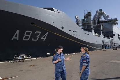 2 marineofficieren met elkaar in gesprek op een kade voor marineschip.