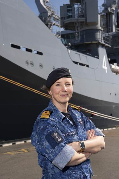 Een marineofficier poseert op de kade voor een schip.