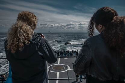 2 meiden kijken uit op het achterdek en de zee en maken foto’s van een FRISC.