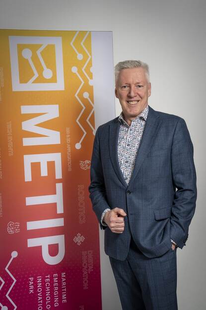 Man in pak staat voor banner en kijkt lachend in de camera.