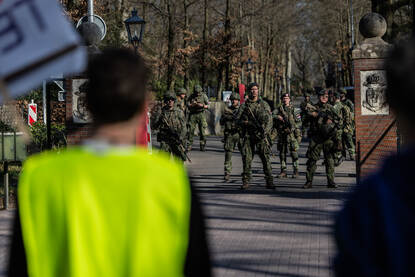 Groepje demonstranten met spandoeken staat bij ingang oog in oog met gewapende militairen