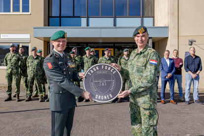 Luitenant-generaal Jan Swillens houdt, samen met brigadegeneraal Joland Dubbeldam een plakkaat in de handen, waarop ‘task force drones’ staat. Achter hen staan militaire en burgercollega’s opgesteld.